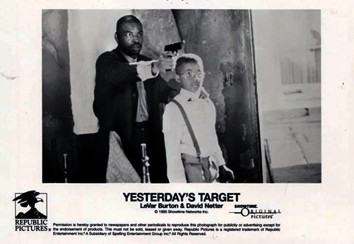 Lavar Burton (as Winstrom) aims a pistol with one hand and rests the other on the shoulder of David Netter (as young Roland).