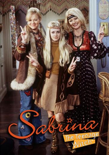 On the set of Sabrina’s house, Caroline Rhea (as Hilda), Melissa Joan Hart (as Sabrina), and Beth Broderick (as Zelda) flash peace signs in sixties clothes.
